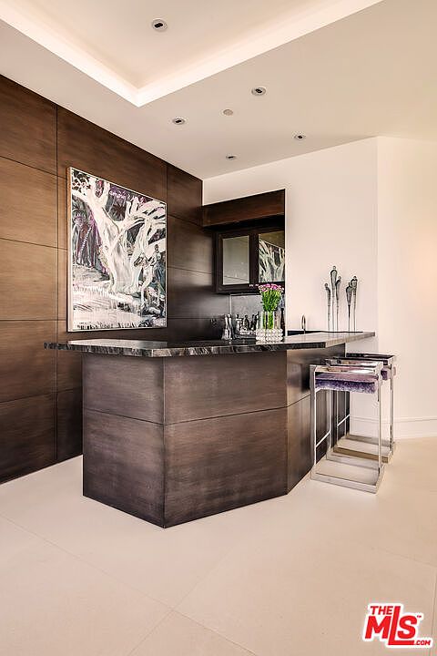 This interior shot showcases a sophisticated wine cellar featuring dark wood paneling and a striking piece of art. A sleek bar area with a dark countertop and modern stools provides a space for tasting and entertaining. The overall ambiance is luxurious and inviting, perfect for a discerning homeowner.