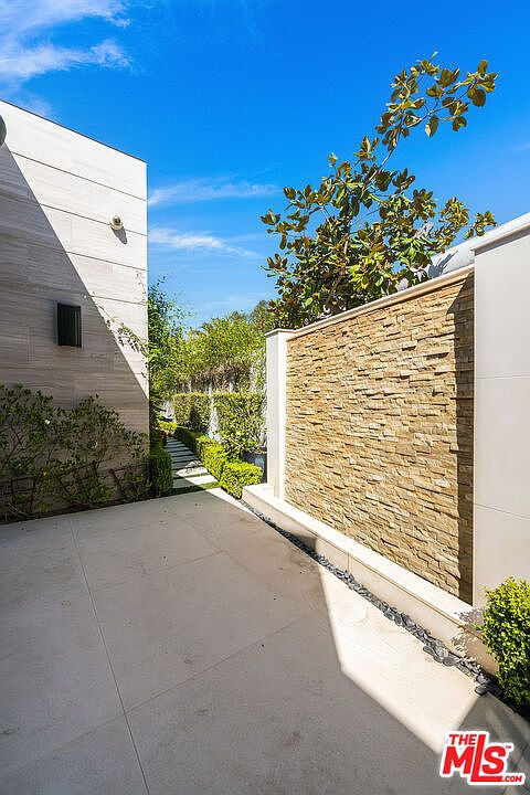This image showcases a modern yard/garden area with a sleek, contemporary design. The space features a stone accent wall, manicured greenery, and a paved walkway, creating a serene and sophisticated outdoor environment. The clean lines and minimalist aesthetic enhance the property's appeal.