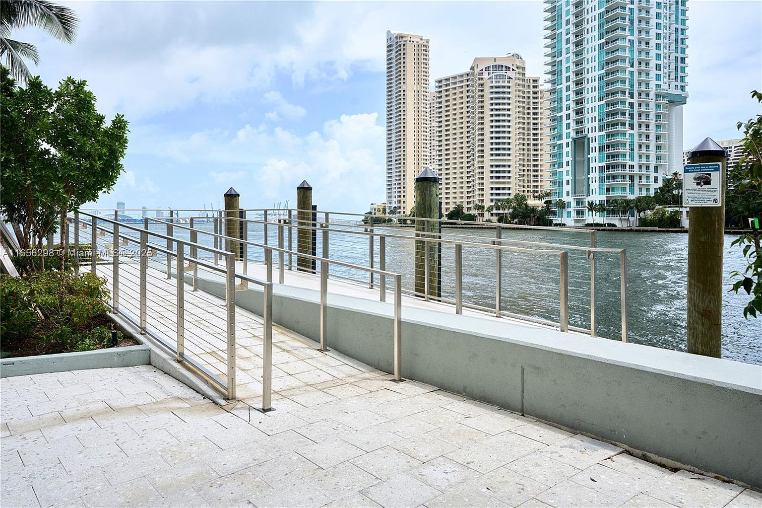 This image showcases a waterfront patio or deck area with modern stainless steel railings and a paved surface. In the background, there are high-rise buildings, suggesting an urban waterfront location. The scene conveys a sense of luxury and relaxation, ideal for enjoying waterfront views.