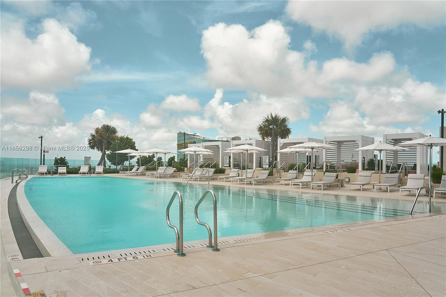 The image showcases a luxurious outdoor pool area, complete with lounge chairs, umbrellas, and cabanas, suggesting a resort-style living experience. The pool's clear blue water reflects the sky, creating a serene and inviting atmosphere. The surrounding architecture appears modern and upscale, enhancing the property's appeal.