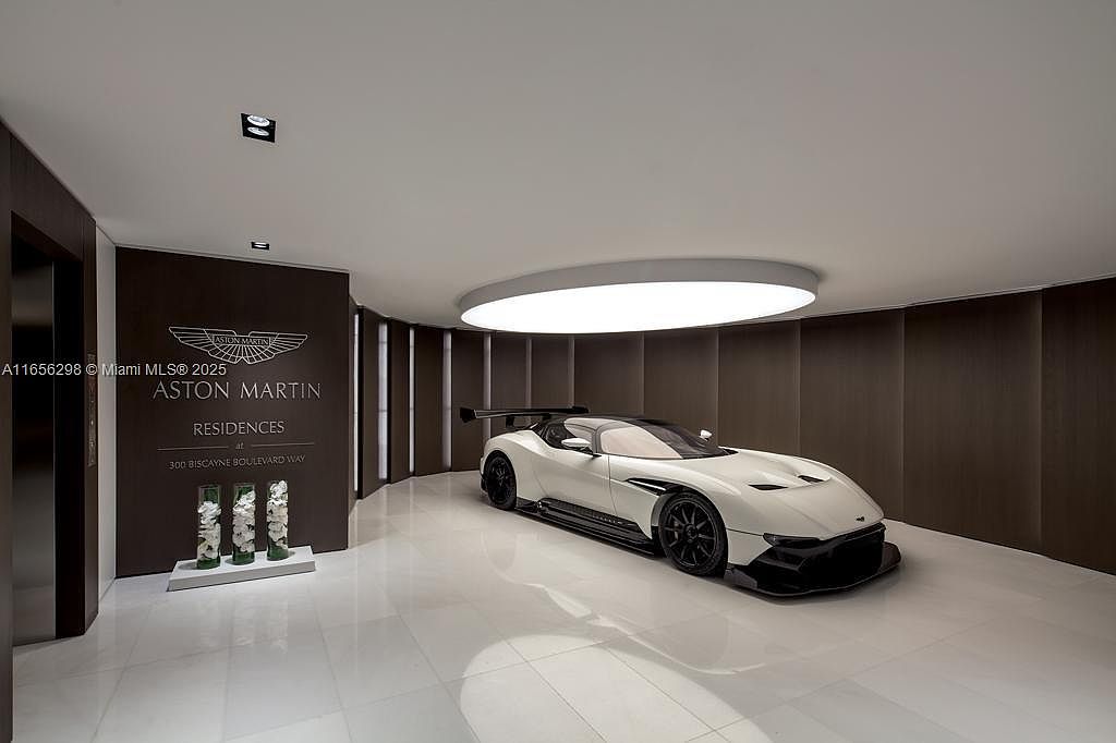 This interior shot showcases a modern hallway featuring a sleek white Aston Martin sports car as a focal point. The hallway is illuminated by a circular ceiling light and features dark wood paneling, creating a sophisticated and luxurious atmosphere. The glossy tiled floor reflects the light, enhancing the sense of space and elegance.