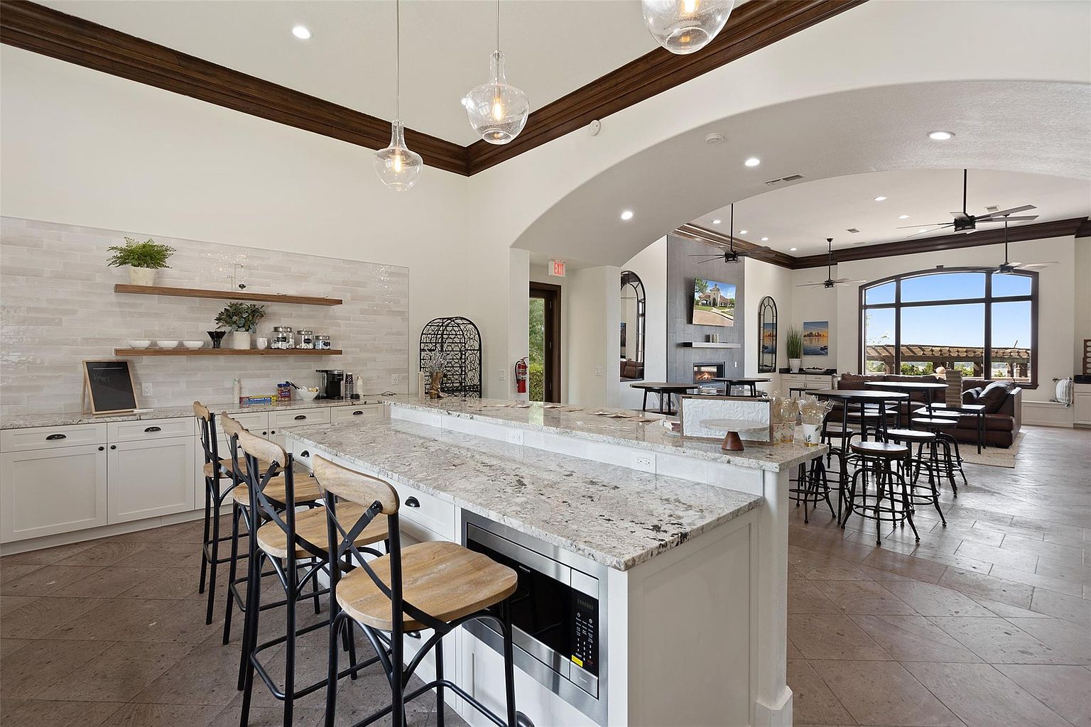 This image showcases a clubhouse amenity, featuring a kitchen area with bar seating and a spacious lounge area. The kitchen boasts white cabinetry, granite countertops, and modern appliances, while the lounge area offers comfortable seating and large windows with scenic views. The overall design is open and inviting, perfect for community gatherings and relaxation.