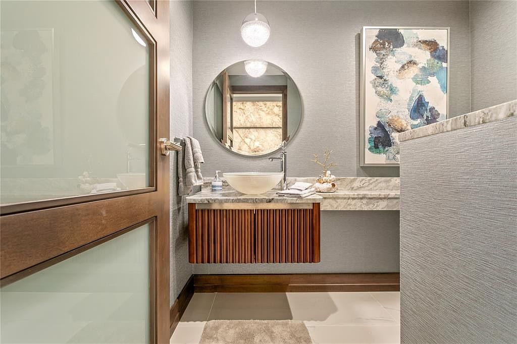 This is a stylish guest bathroom featuring a modern vanity with a vessel sink and a round mirror. The walls are painted in a soft gray, complemented by a piece of abstract art. The room is well-lit with a pendant light, creating a clean and inviting space.