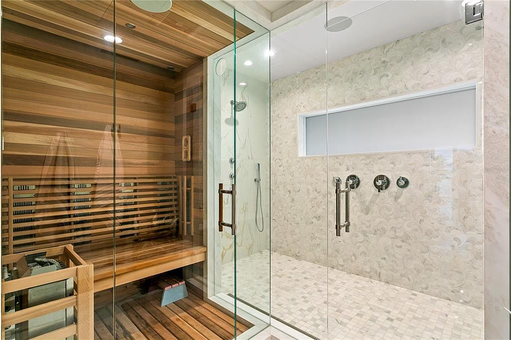 This is a luxurious primary bathroom featuring a sauna and a glass-enclosed shower. The sauna is constructed with light-colored wood and has built-in benches. The shower features marble-like tile, a rainfall showerhead, and modern fixtures, creating a spa-like atmosphere.