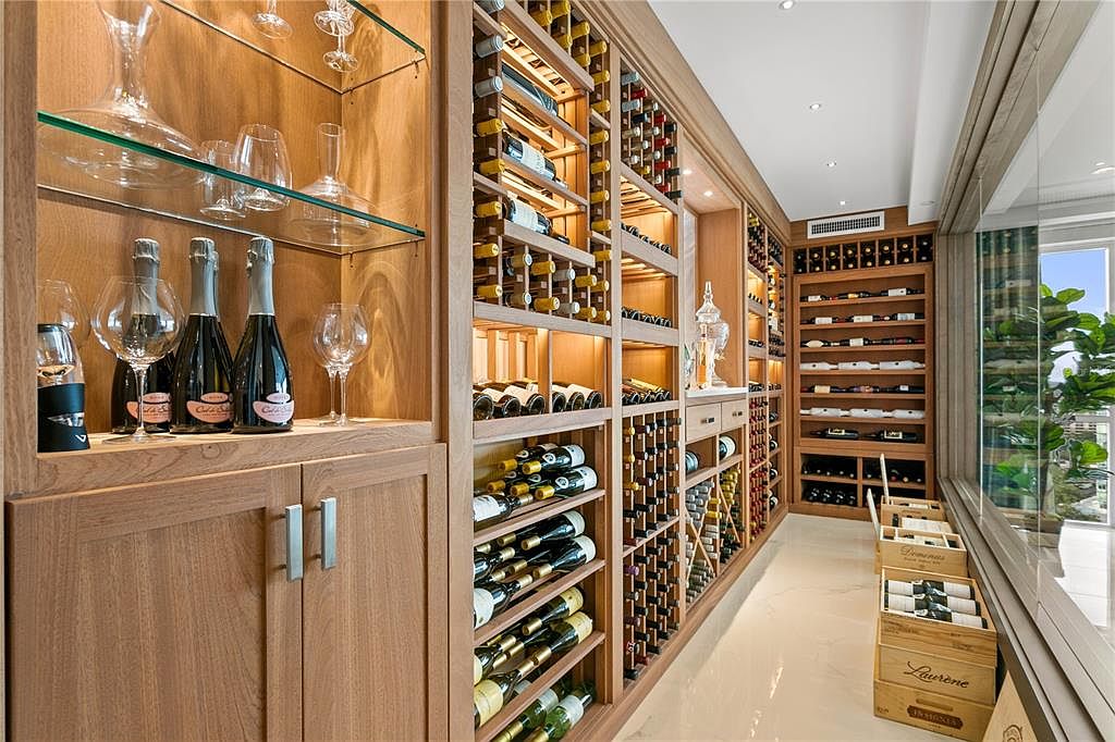 This image showcases a well-stocked wine cellar with custom wooden shelving designed to hold numerous bottles. The cellar features a variety of wines, glassware, and decorative elements, creating an elegant and sophisticated space for wine storage and display. Natural light filters in from a nearby window, enhancing the ambiance.