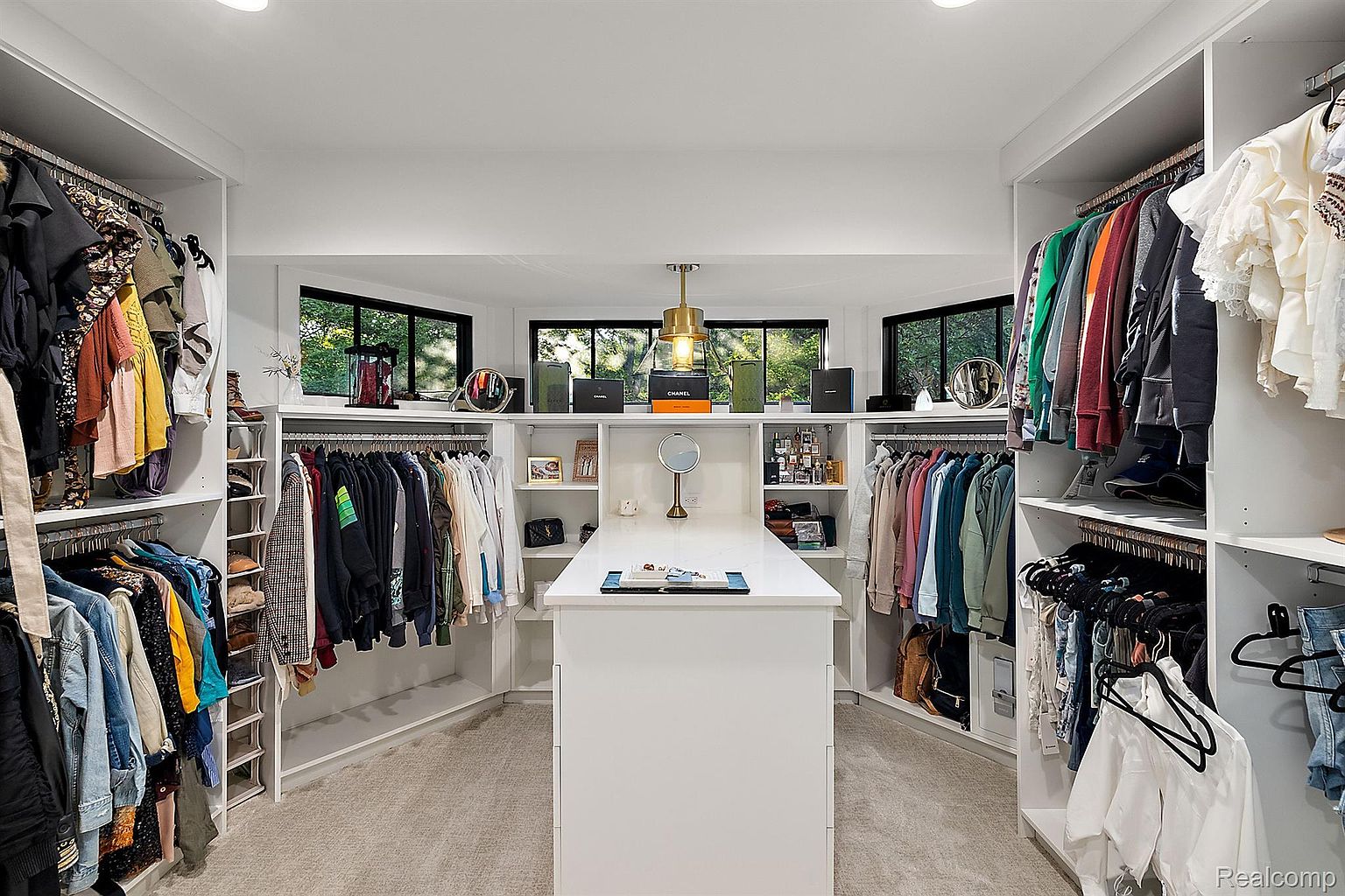 This is a spacious walk-in closet featuring custom shelving and hanging rods for organized storage. A central island provides additional surface space, and windows offer natural light. The closet is designed with a clean, modern aesthetic, enhancing the appeal for potential buyers.