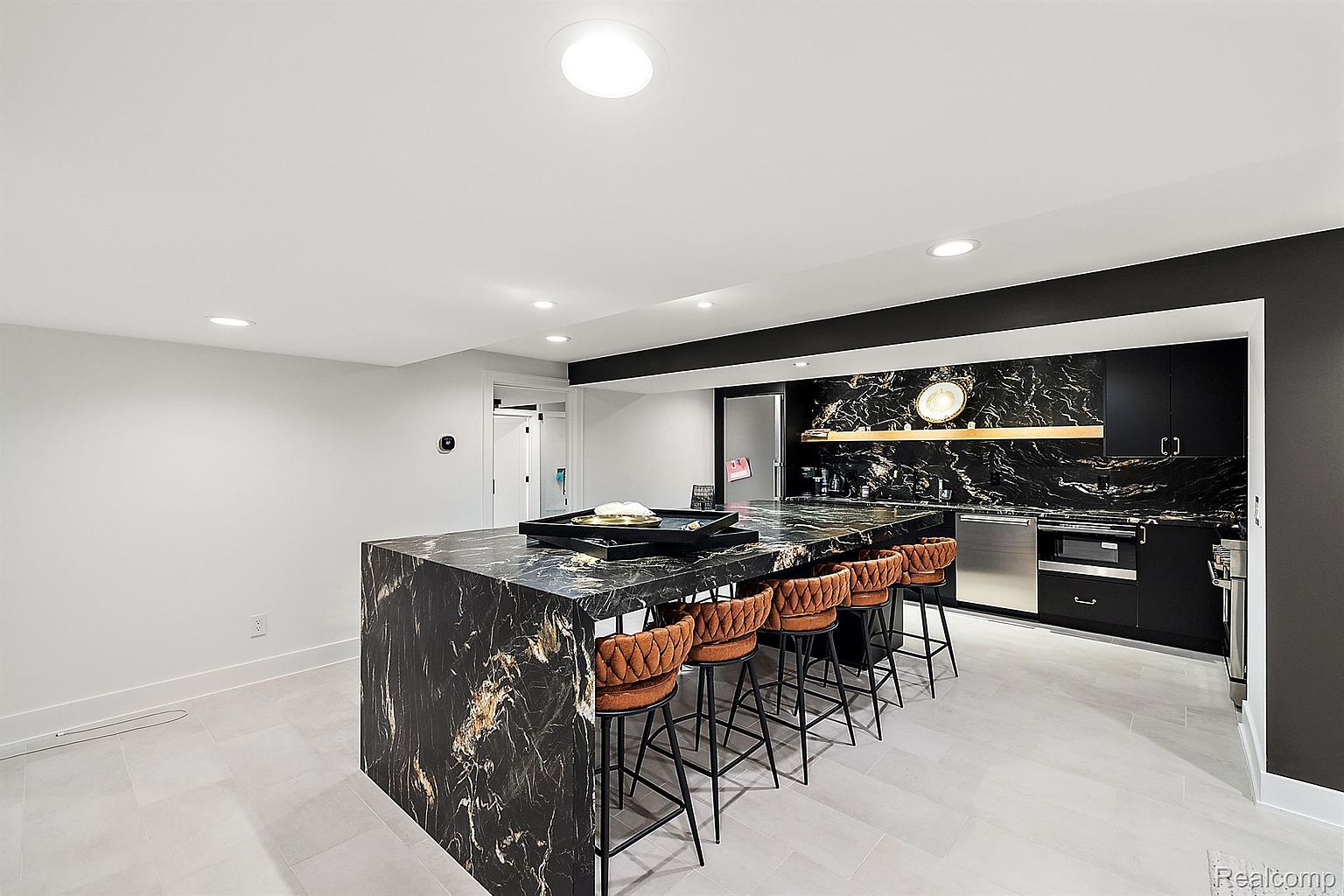 This is a modern kitchen featuring a large island with a black marble countertop and seating for six. The kitchen also has black cabinetry, stainless steel appliances, and a black marble backsplash. The overall style is sleek and contemporary, with a focus on high-end finishes.