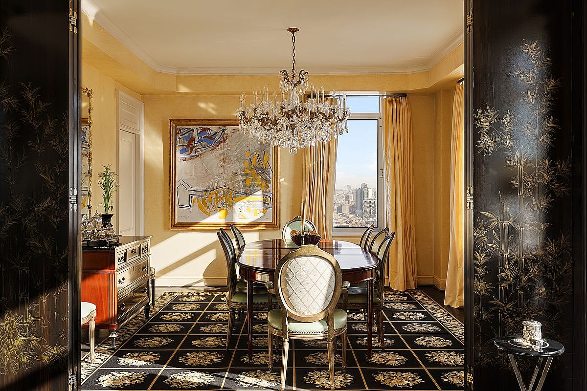 This elegant dining room features a formal mahogany table surrounded by upholstered chairs, set beneath a grand crystal chandelier. The space is framed by dramatic black lacquer doors with gold bamboo motifs, opening into a room with warm yellow walls, a patterned black and gold rug, and a large abstract painting. A window at the far end provides a stunning urban cityscape view, creating a sophisticated and luxurious atmosphere.