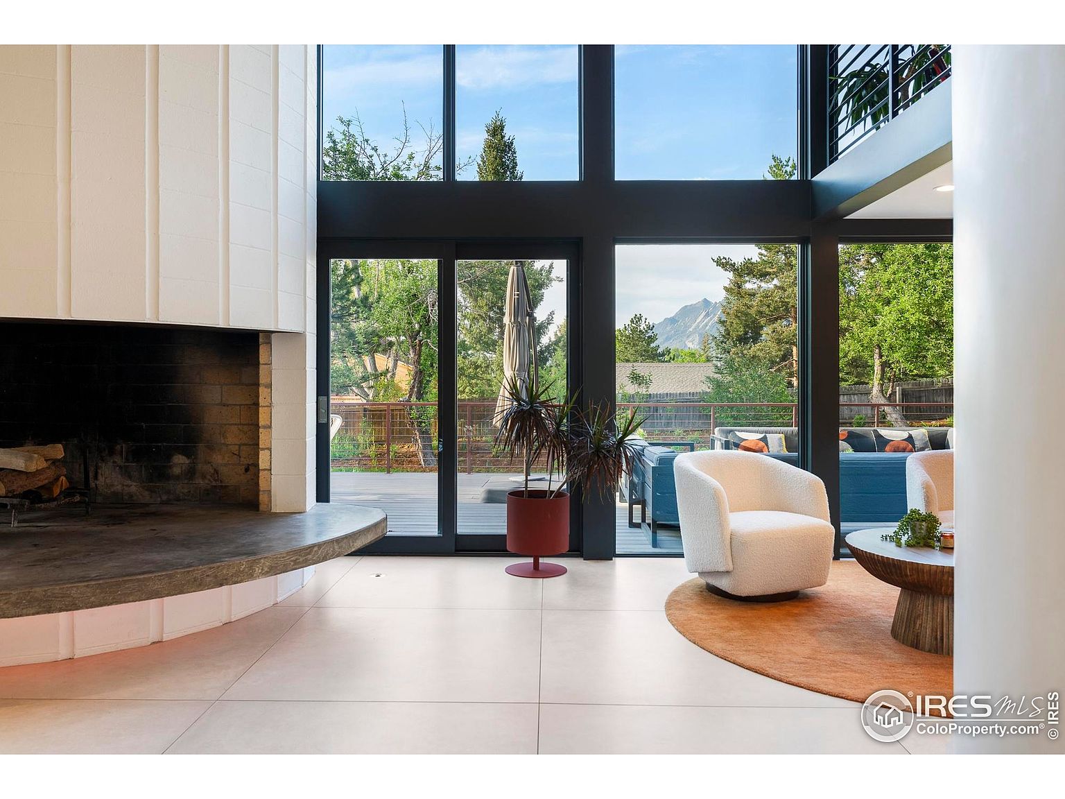 This is an interior shot of a living room featuring a modern fireplace, large windows with views of the outdoors, and stylish furniture. The room has a bright and airy feel, with a neutral color palette and a focus on natural light. The open floor plan and contemporary design make it an inviting space.