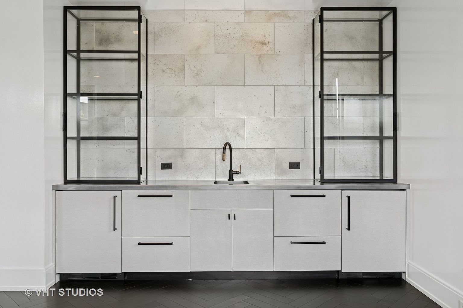 This interior shot showcases a modern kitchen area with a sleek design. The focal point is a countertop with a sink and faucet, flanked by cabinets and drawers with minimalist hardware. Above the countertop are two tall, glass-fronted cabinets, adding a touch of elegance and display space.