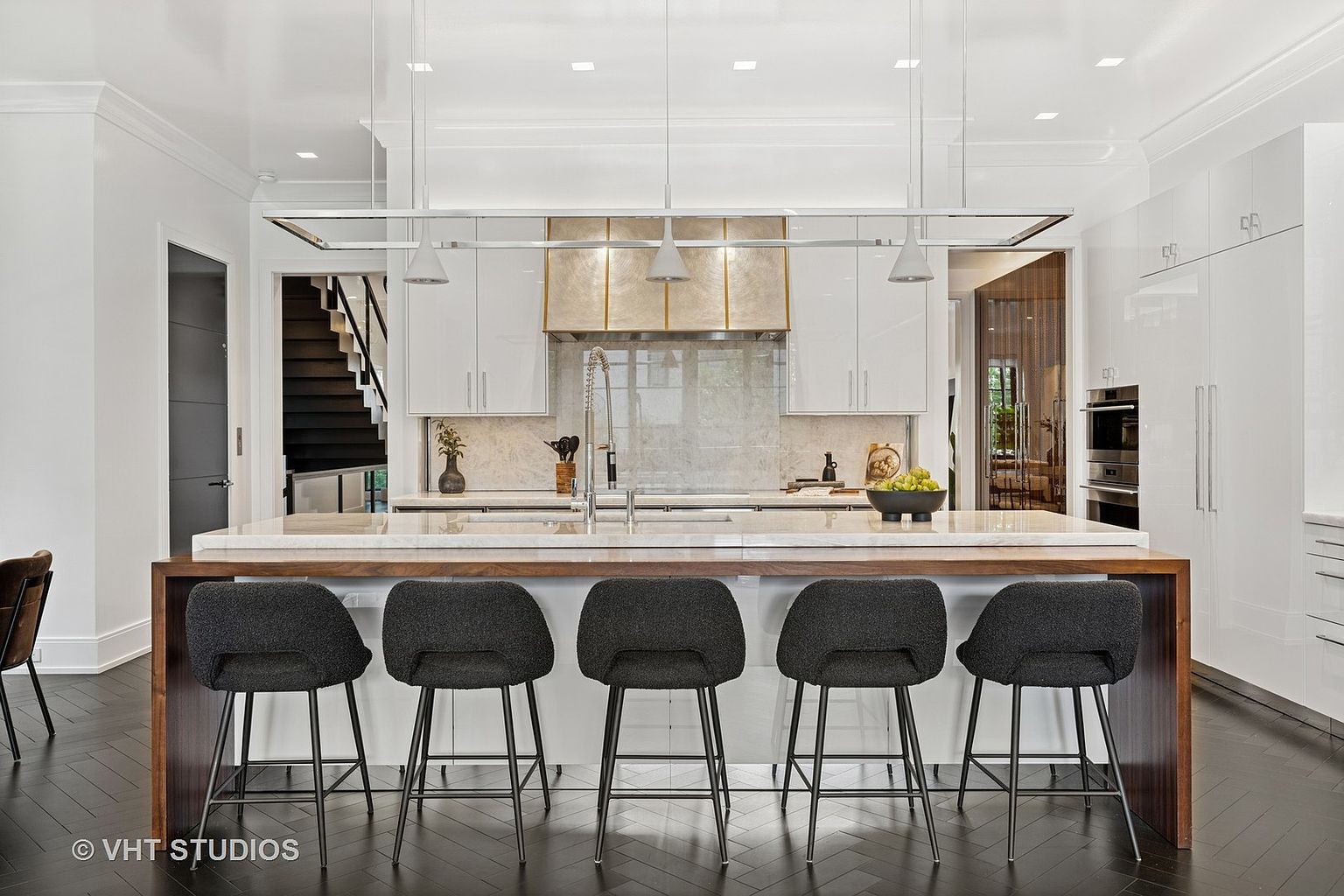 This is a modern kitchen featuring a large island with seating for five, white cabinetry, and stainless steel appliances. The kitchen has a clean and contemporary style, with a focus on functionality and design. The dark wood floors add a touch of warmth to the space.