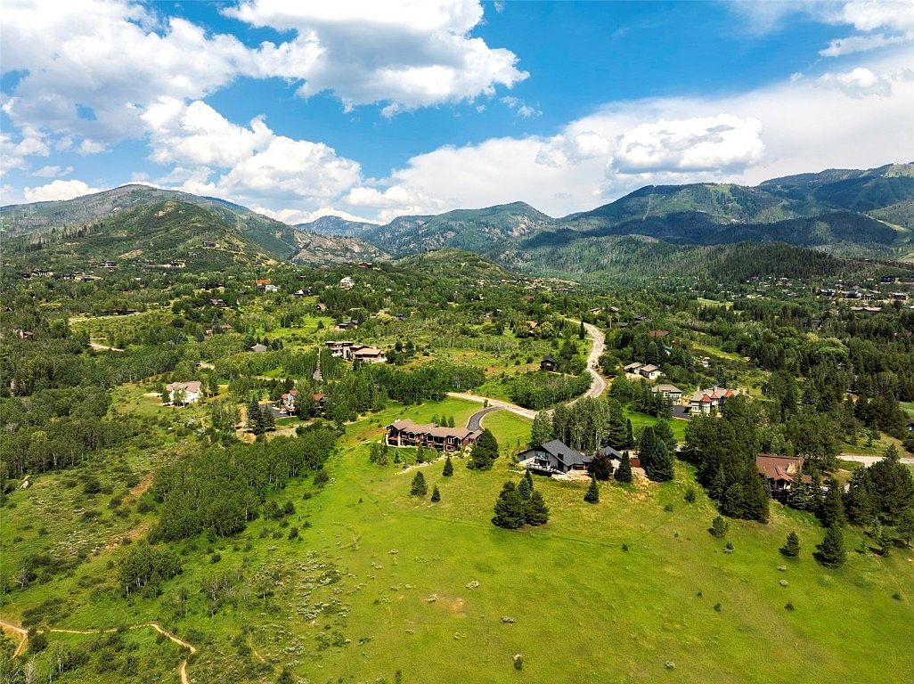 This aerial shot showcases a sprawling estate nestled in a lush, green landscape with mountains in the background. Several large homes are visible, each with well-maintained yards and mature trees, suggesting a private and upscale community. The overall impression is one of tranquility and luxury, highlighting the property's desirable location and spacious surroundings.