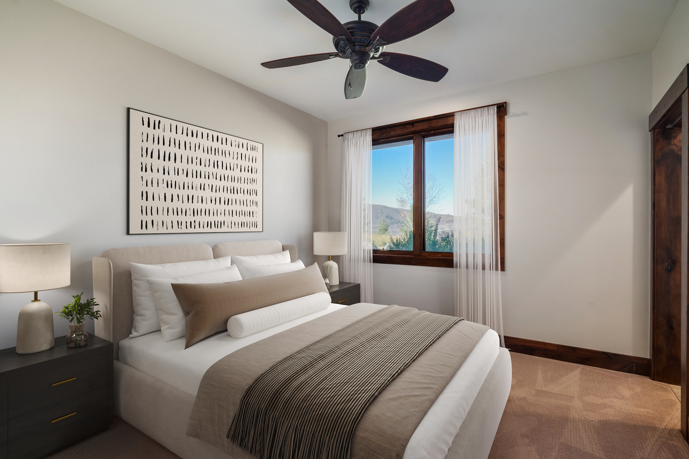 This is a tastefully decorated guest bedroom. The room features a comfortable bed with neutral-toned bedding, a modern art piece above the headboard, and a window with sheer curtains that allows natural light to filter in. The dark wood trim around the window and door add a touch of rustic charm.