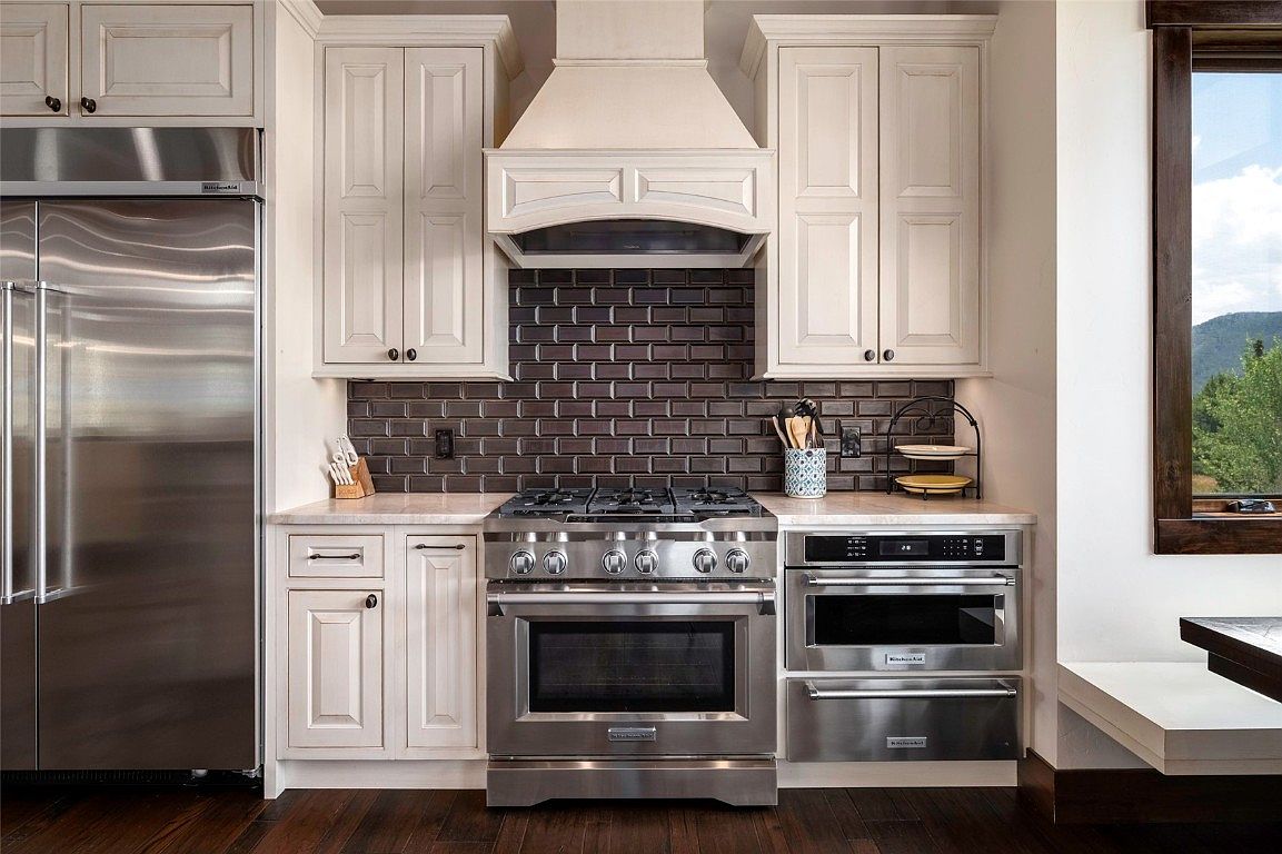 This is a well-appointed kitchen featuring stainless steel appliances, including a refrigerator, oven, and microwave. The cabinetry is a light, neutral color, complemented by a dark backsplash. The kitchen is well-lit and appears to be in excellent condition, offering a modern and functional space.