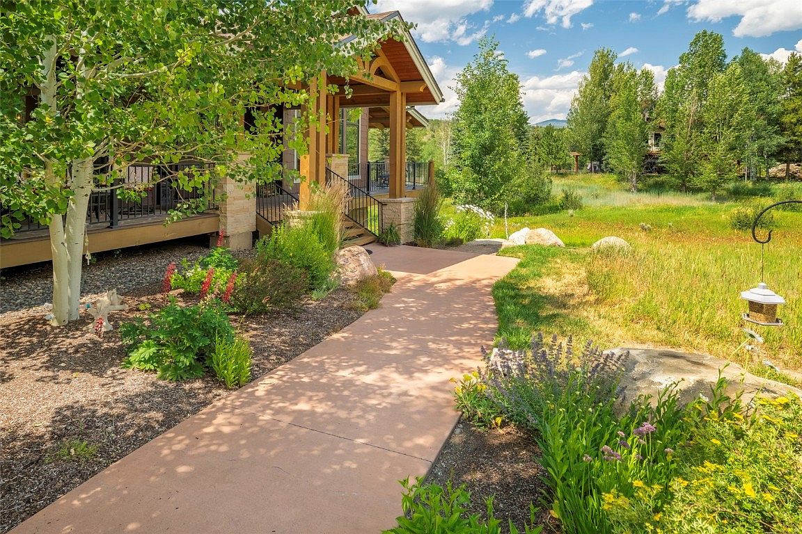 This image showcases a beautifully landscaped yard and garden leading up to a home's porch. A stone pathway meanders through lush greenery, colorful flowers, and mature trees. The scene evokes a sense of tranquility and highlights the property's well-maintained outdoor space, enhancing its curb appeal.