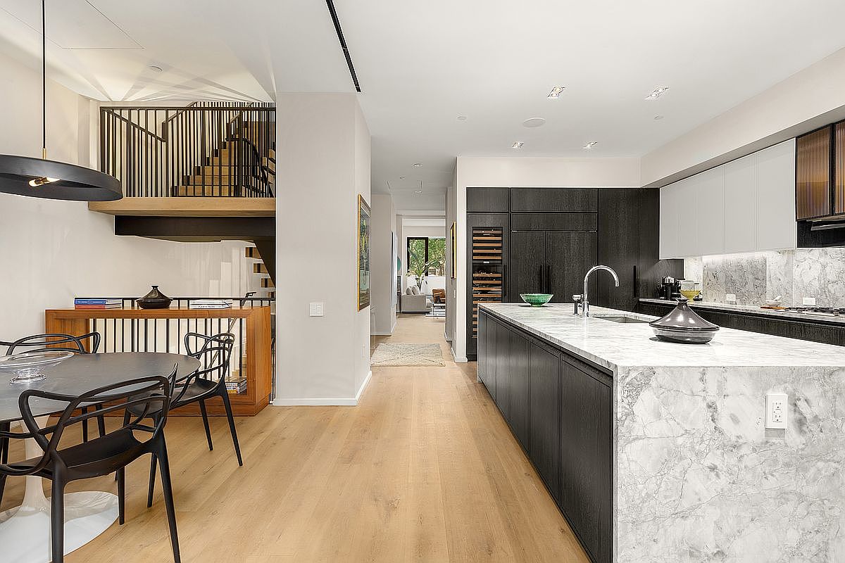 This is a modern kitchen with a large marble island and dark wood cabinetry. The kitchen features stainless steel appliances and a sleek design. The open floor plan connects the kitchen to the dining area and hallway, creating a spacious and inviting atmosphere.