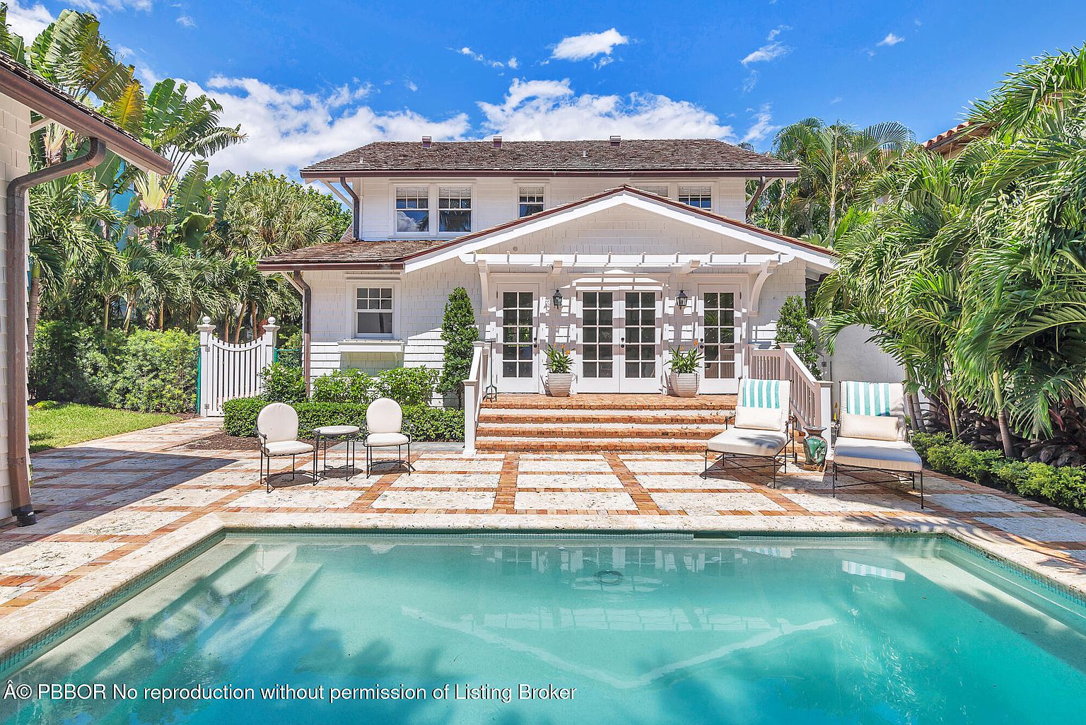 This image showcases the rear exterior of a beautiful two-story home, highlighting its inviting pool area. The pool is surrounded by a brick-laid patio, with comfortable lounge chairs and seating areas arranged for relaxation. The house features a charming pergola over the entrance, adding to the overall appeal of this outdoor living space.