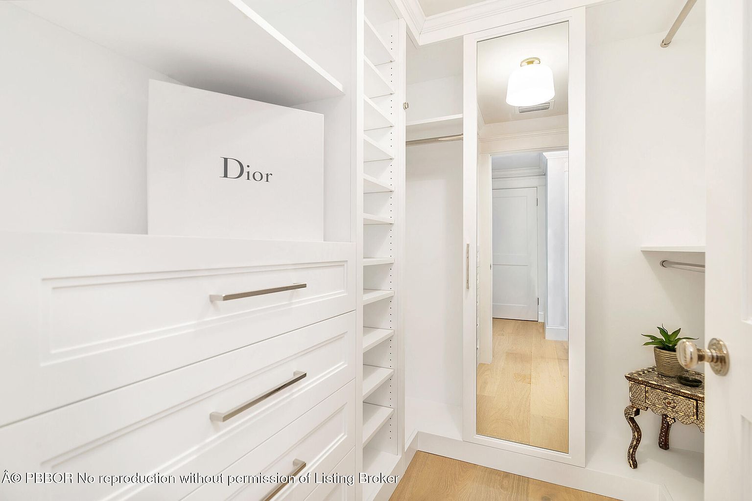 This is a bright and organized walk-in closet featuring custom white cabinetry, drawers with sleek silver hardware, and adjustable shelving. A full-length mirror adds depth and functionality to the space. The closet is well-lit and appears spacious, offering ample storage.