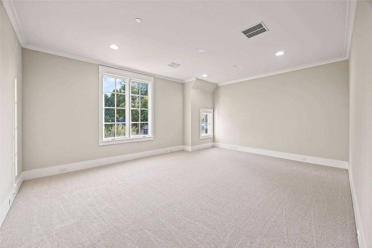This is a spacious, well-lit bedroom featuring neutral-toned walls, white trim, and plush carpeting. A large window provides ample natural light and a view of the outdoors. The room is clean and uncluttered, presenting a blank canvas for potential buyers to envision their own personal style.