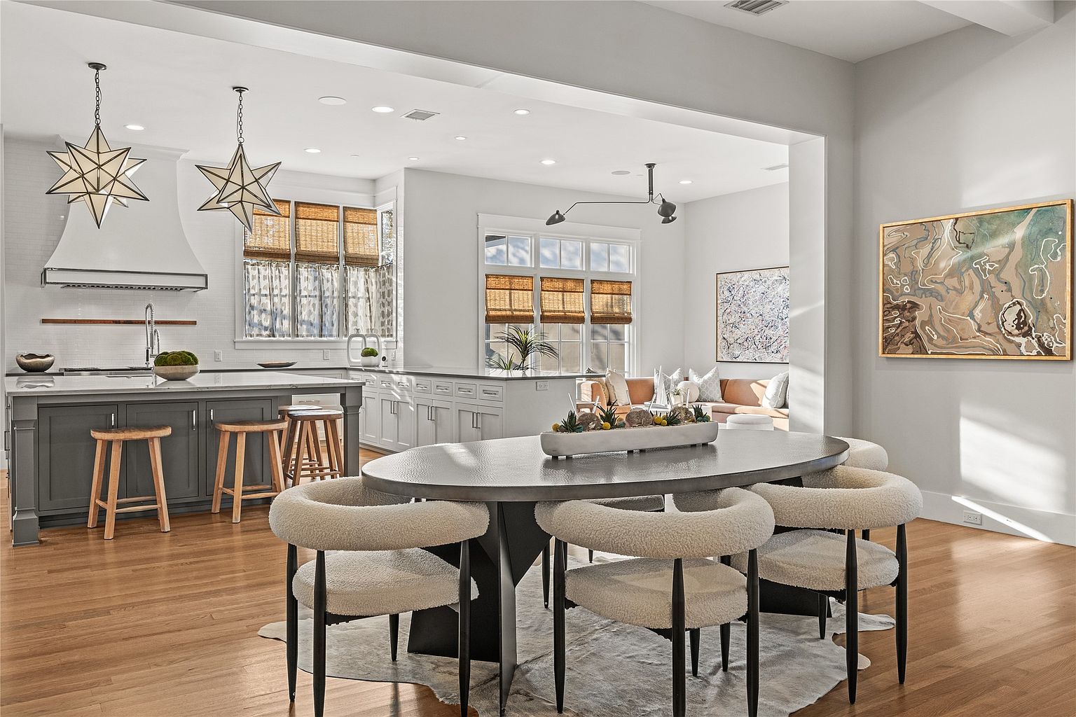 This interior shot showcases a modern dining area adjacent to a kitchen and living space. The dining area features an oval table with unique chairs, set upon a cowhide rug, with a decorative centerpiece. The open-concept design allows for seamless flow between the spaces, enhancing the home's appeal for entertaining and everyday living.