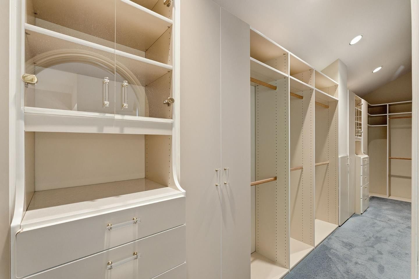 This is a well-organized walk-in closet featuring custom shelving and storage solutions. The closet is painted in a neutral color, with ample hanging space and drawers. The overall impression is clean, spacious, and designed for efficient storage.