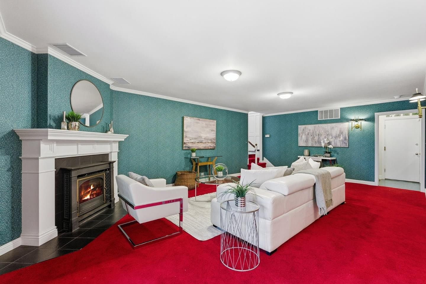 This is an interior shot of a living room featuring a white sofa and armchair, a fireplace with a white mantel, and teal wallpaper. The room is carpeted in red, and there are several tables and decorative items. The overall impression is a mix of classic and modern styles.