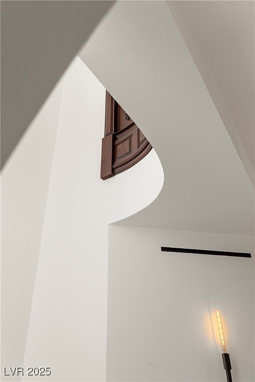 This image showcases a modern architectural detail, featuring a curved wall and ceiling design with a glimpse of a dark wood element, possibly a door or decorative panel. The stark white walls contrast with the dark accent, creating a visually striking and minimalist aesthetic. A sleek, linear light fixture adds to the contemporary feel of the space.