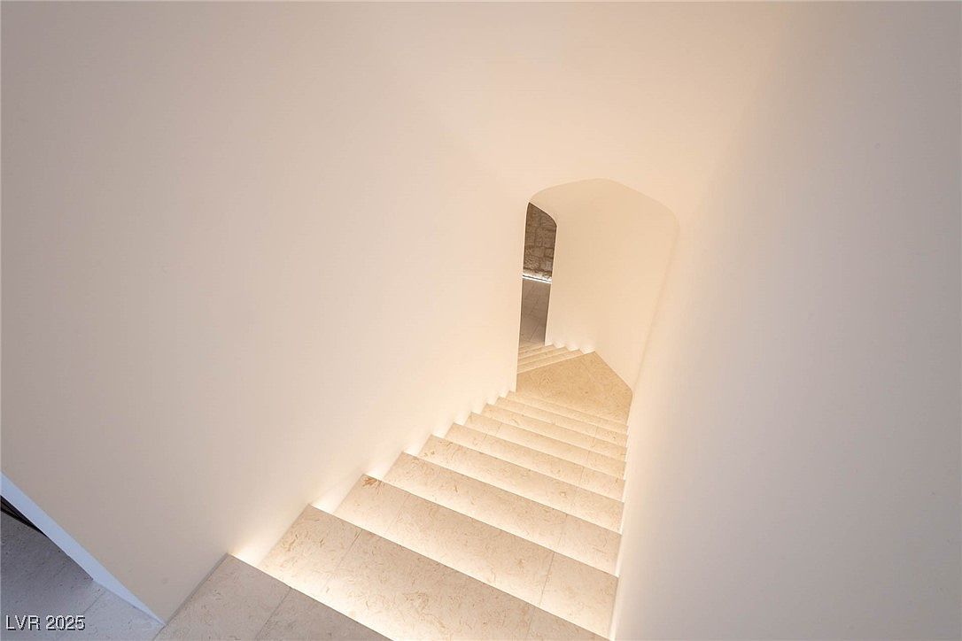 This image showcases a modern interior staircase with a minimalist design. The stairs are illuminated with subtle lighting, highlighting the clean lines and smooth surfaces. The walls are painted in a neutral tone, creating a bright and airy atmosphere, and the curved architectural detail adds a touch of elegance.