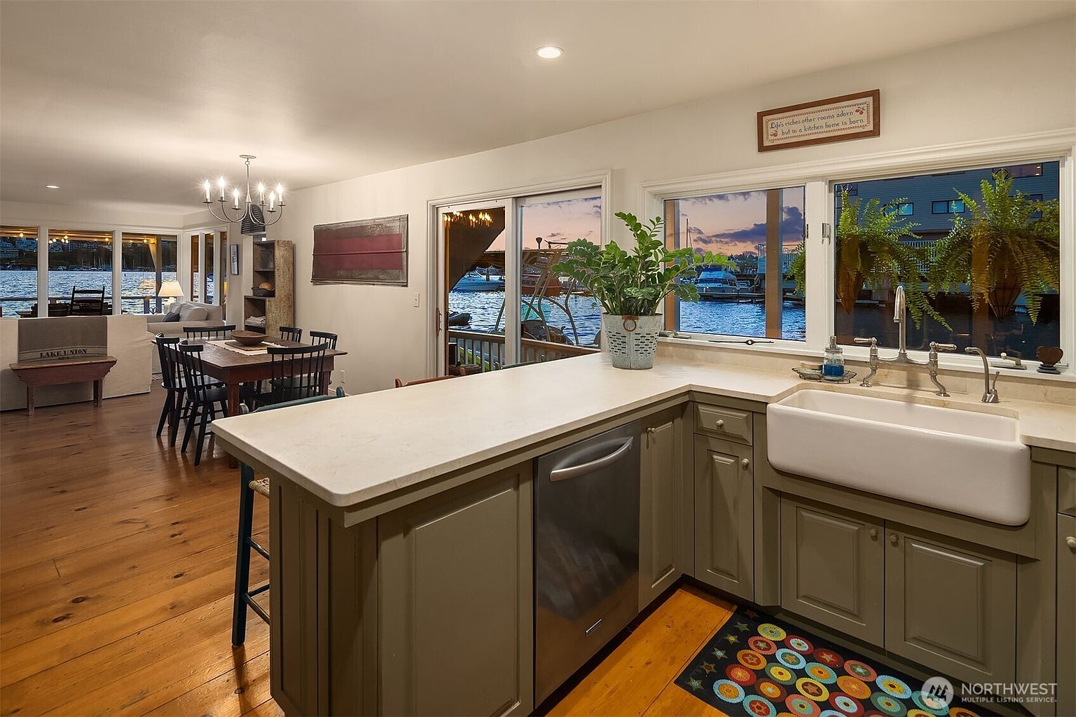 This interior shot showcases a charming kitchen with a view of the water. The kitchen features a farmhouse sink, stainless steel appliances, and warm-toned cabinetry. The open layout connects the kitchen to a dining area and living room, creating a welcoming and spacious atmosphere with natural light.