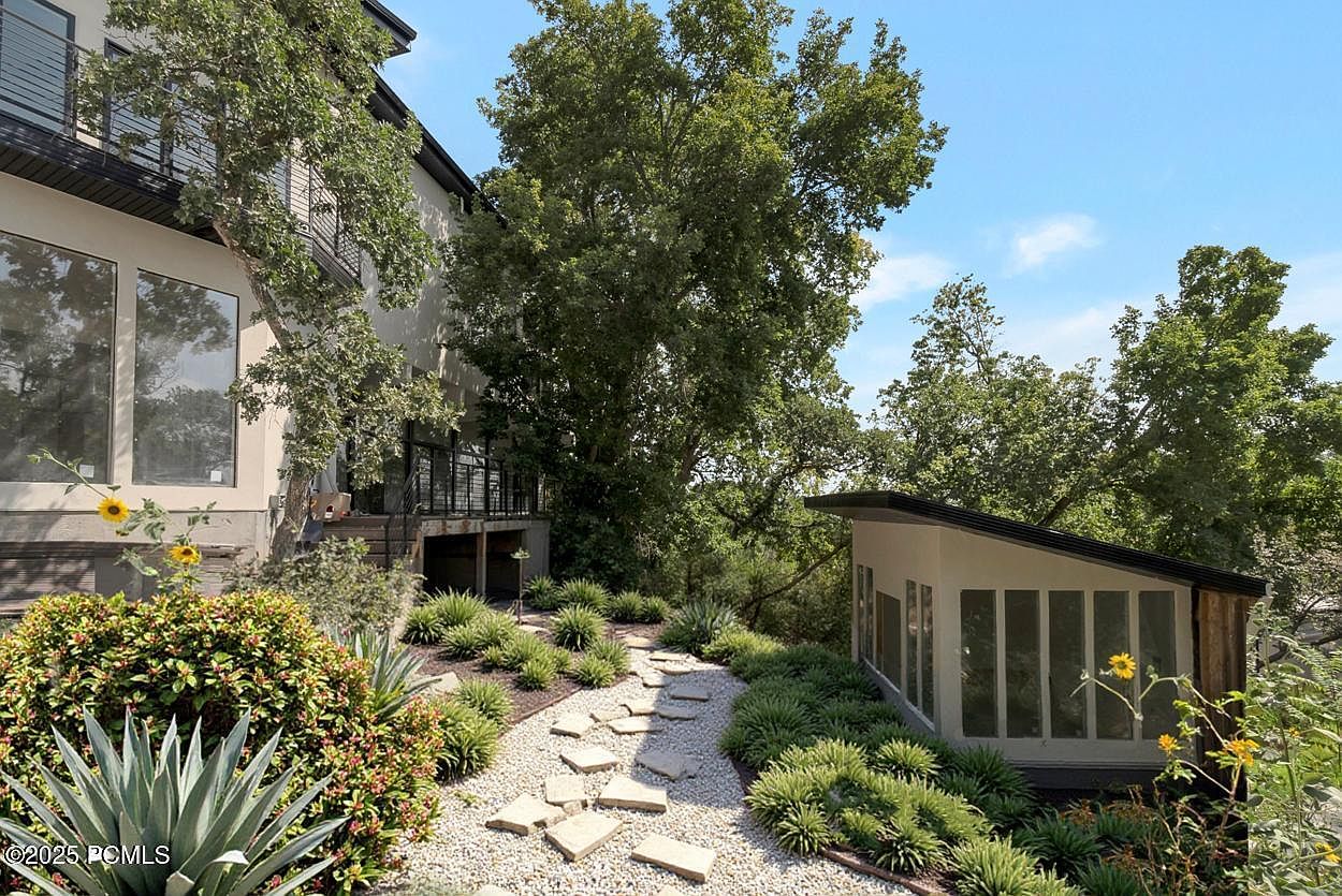 This image showcases a beautifully landscaped yard with a stone pathway leading towards a modern outbuilding. Lush greenery and carefully arranged plants create a serene and inviting atmosphere. The pathway is made of light-colored stones and gravel, adding texture and visual interest to the garden.