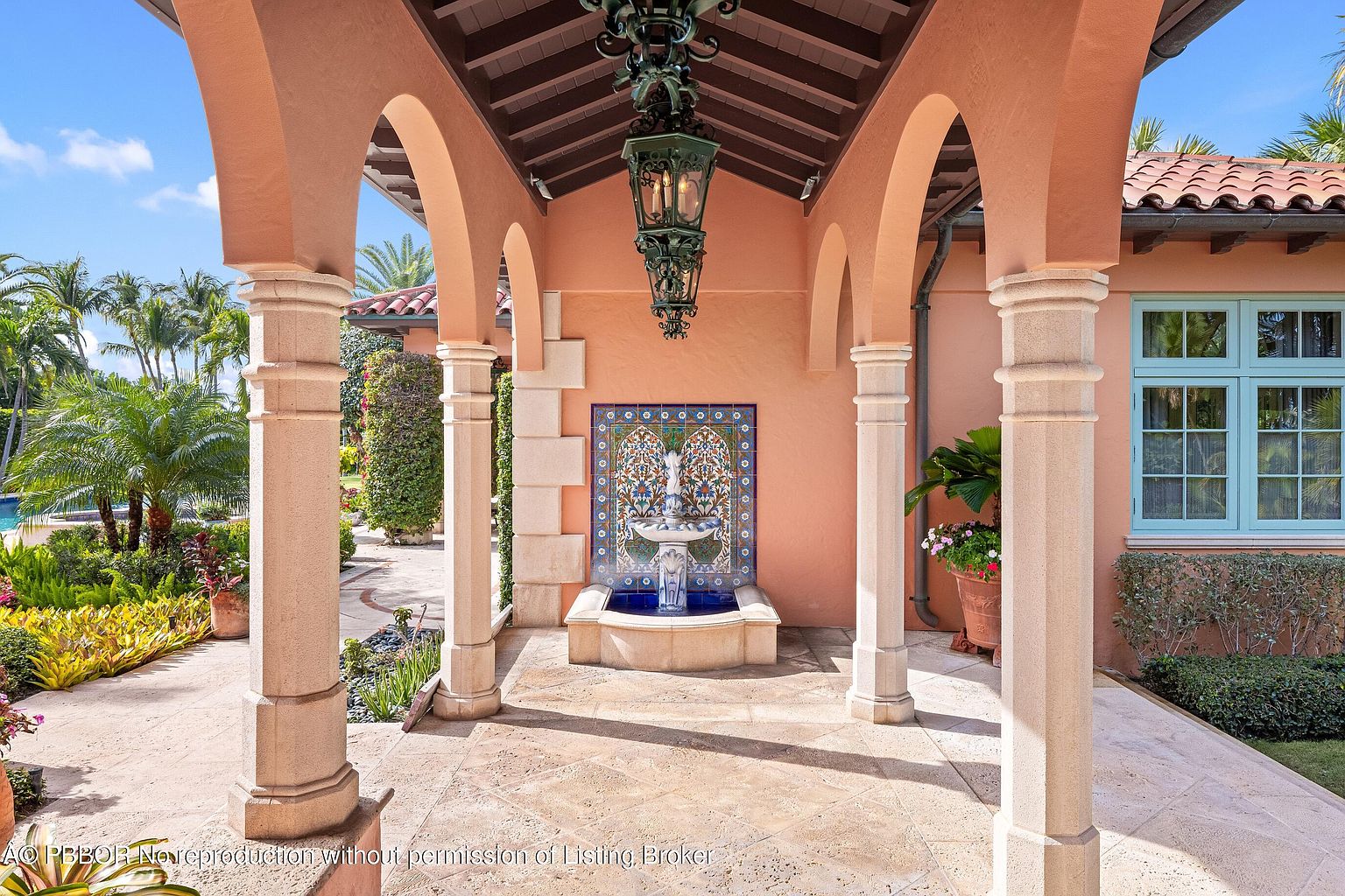 This image showcases an elegant entryway featuring a series of arched columns leading to a decorative fountain with a tiled backdrop. The architecture is reminiscent of Mediterranean style, with warm-toned walls and a tiled roof visible in the background. The space is well-lit and inviting, creating a sophisticated first impression.