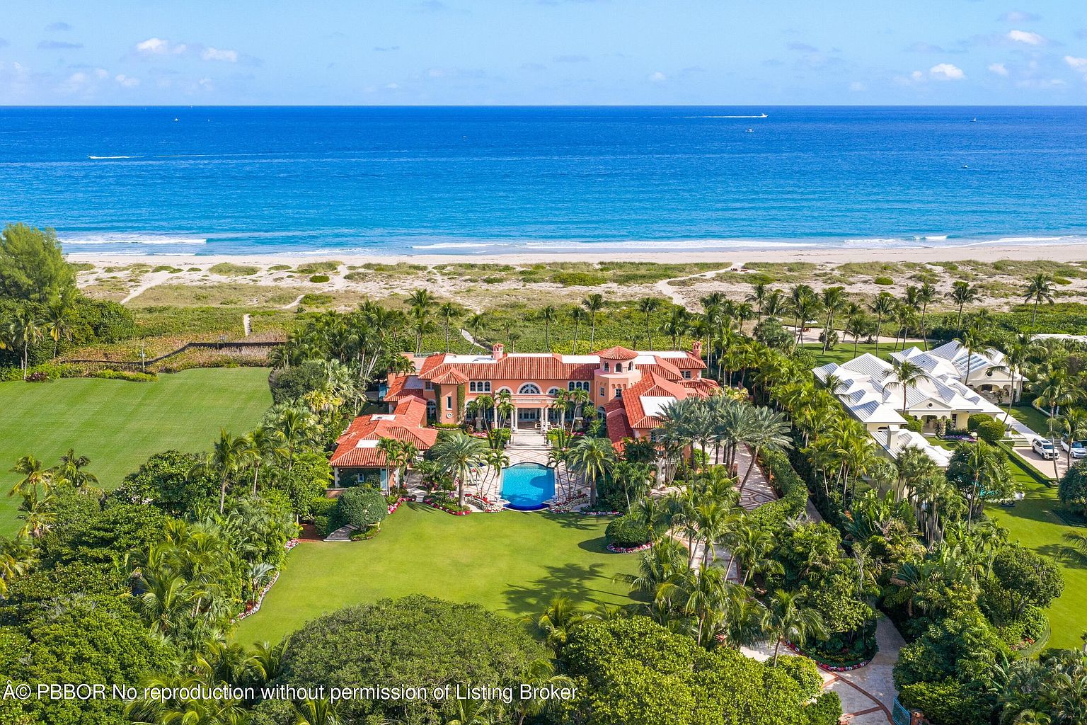 This aerial view showcases a luxurious beachfront estate with a terracotta-tiled roof, a private pool, and meticulously manicured lawns. The property is surrounded by lush tropical landscaping and offers direct access to a pristine sandy beach and the ocean. The overall impression is one of opulence and serene coastal living.