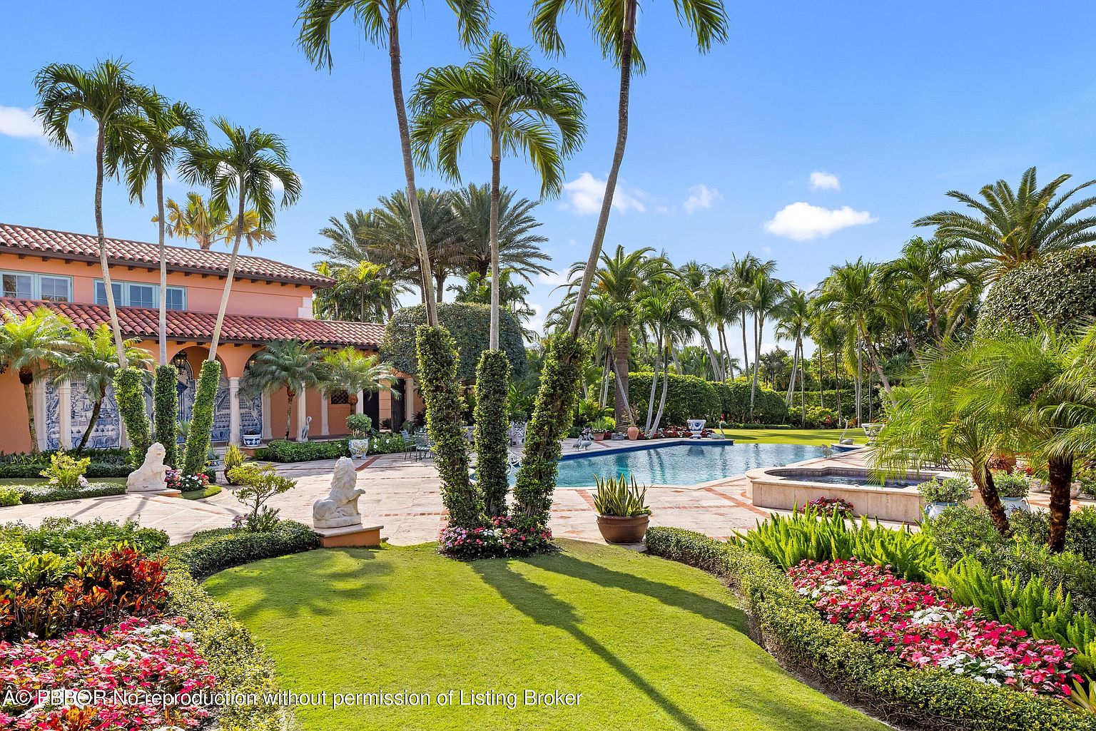 This exterior shot showcases a meticulously landscaped yard and garden, featuring lush green lawns, vibrant flower beds, and mature palm trees. A luxurious pool and spa area are visible in the background, suggesting a private and serene outdoor living space. The overall impression is one of elegance and tranquility, perfect for relaxation and entertainment.