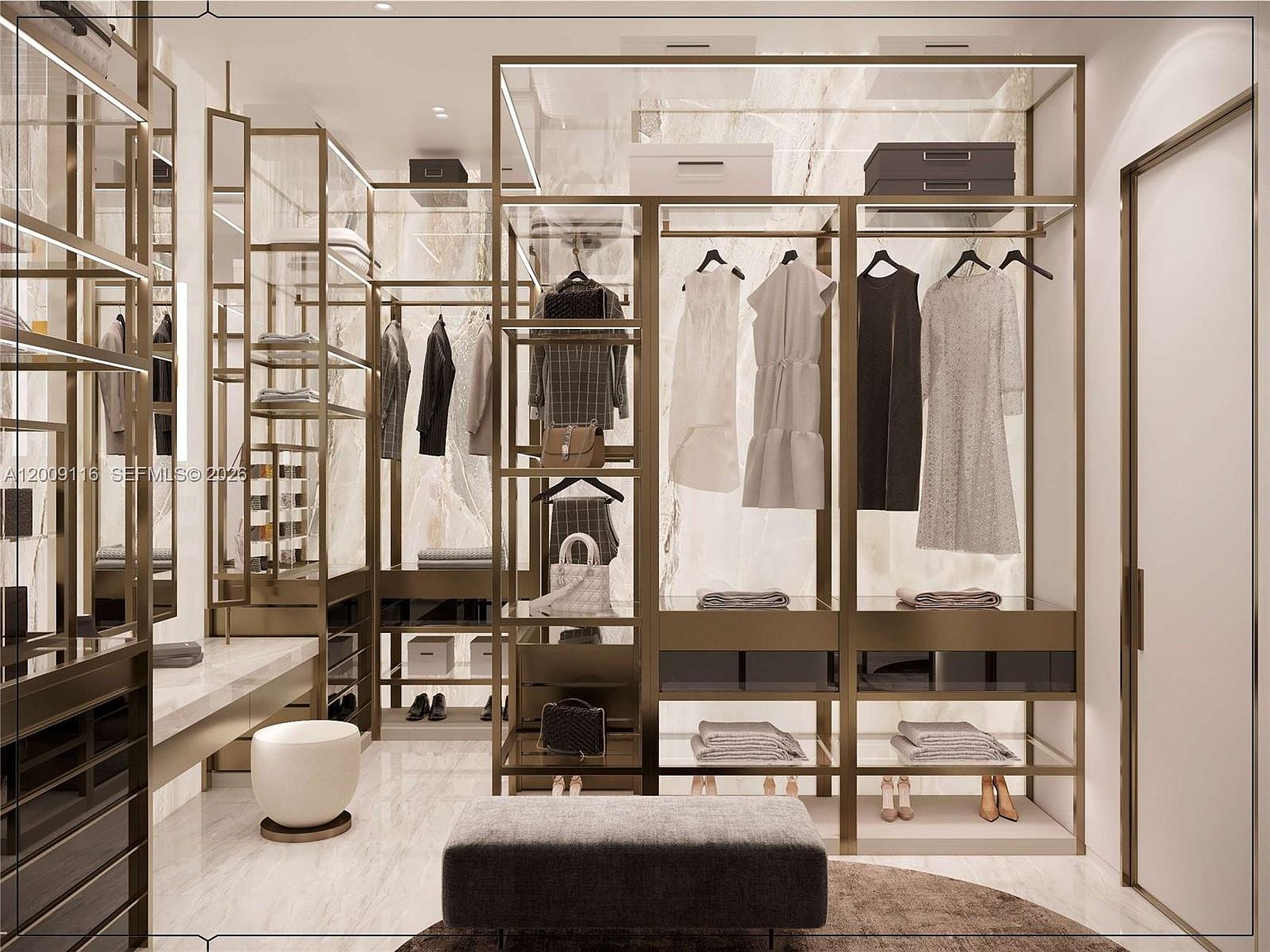 This luxurious walk-in closet features a sophisticated design with gold-toned metal shelving and integrated lighting. The space is accented by a marble-patterned wall, a central grey upholstered ottoman, and a small white stool, creating an organized and high-end boutique atmosphere. The perspective is centered, showcasing the symmetrical layout of the hanging racks, open shelving, and display areas for clothing and accessories.