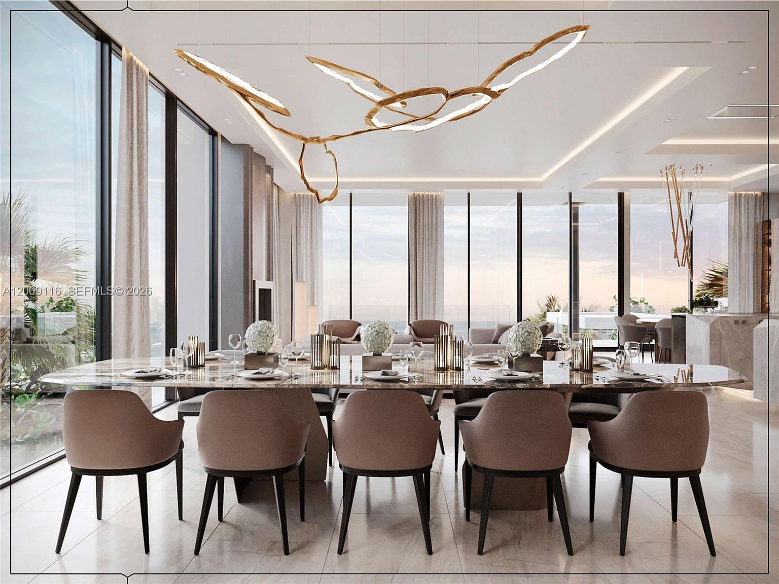 This sophisticated dining room features a long, polished stone-topped table surrounded by ten upholstered chairs with dark legs. A striking, sculptural gold light fixture hangs above the table, serving as a focal point in the open-concept space. The room is framed by expansive, floor-to-ceiling windows that offer panoramic views and fill the area with natural light, creating an airy and luxurious atmosphere.