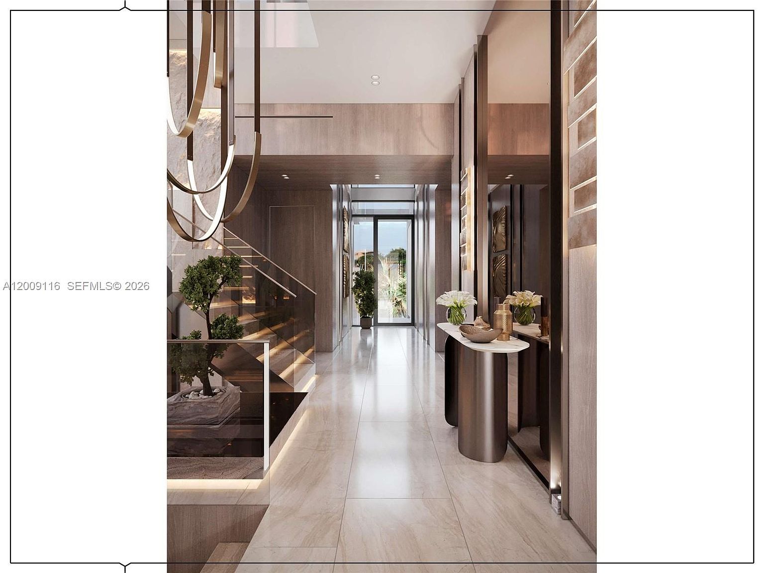 This sophisticated entryway and hallway feature a sleek, modern aesthetic with light-toned stone flooring and warm wood-paneled walls. A sculptural, multi-ring chandelier hangs above a floating console table, while a glass-railed staircase with integrated lighting leads to the upper level. The perspective looks down a long, gallery-like corridor toward a glass door that provides a view of the outdoor greenery.