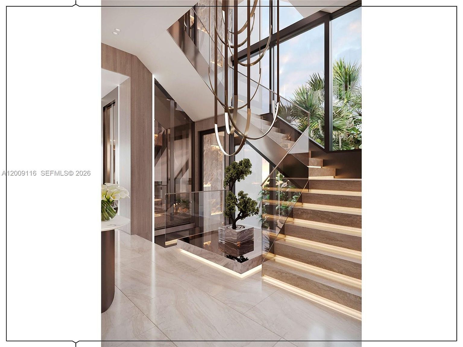 This sophisticated entryway features a grand staircase with illuminated treads and a glass railing, creating a modern and airy aesthetic. A sculptural chandelier hangs from above, casting light over a central decorative tree set on a raised stone platform. Large windows provide a view of lush greenery outside, enhancing the seamless transition between indoor and outdoor spaces.
