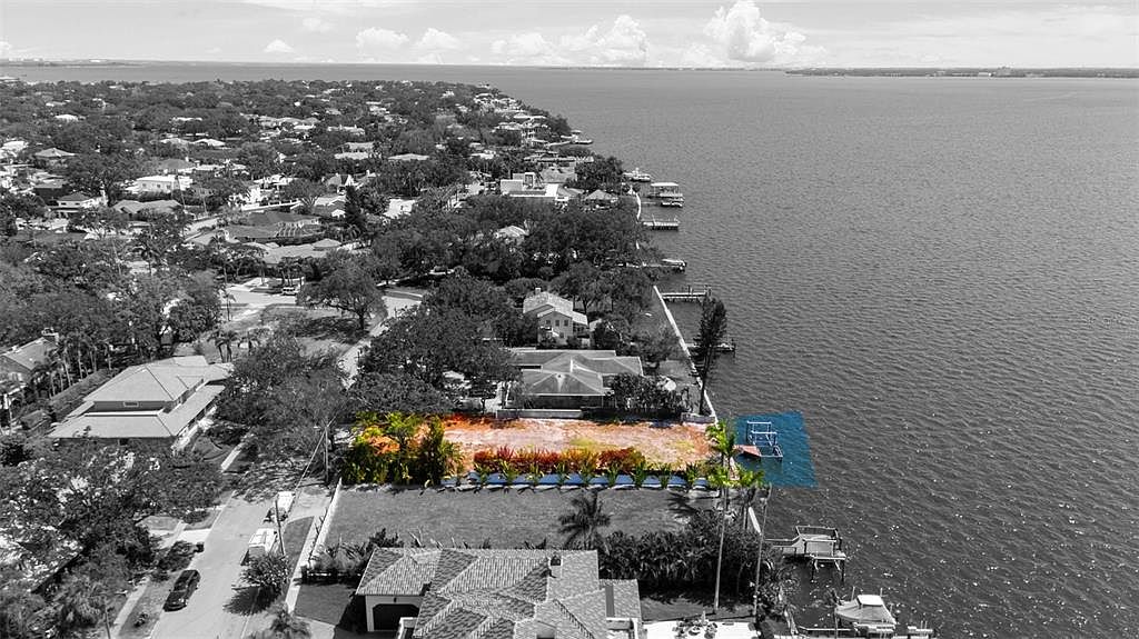 This aerial view showcases a waterfront property with a vacant lot ready for development. The lot is highlighted with an orange overlay, emphasizing its potential, while a blue overlay marks the dock area. The surrounding neighborhood features mature trees and established homes, creating a desirable coastal setting.