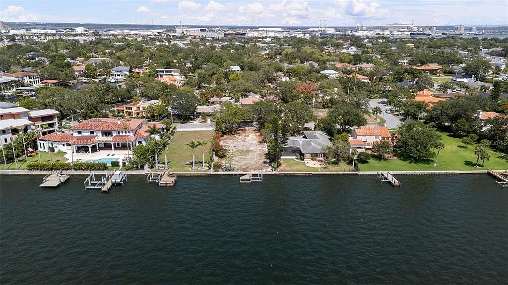 This aerial view showcases waterfront properties with lush landscaping and private docks. The scene captures a mix of residential architecture, with a vacant lot also visible. The overall impression is one of luxury and serene waterfront living.