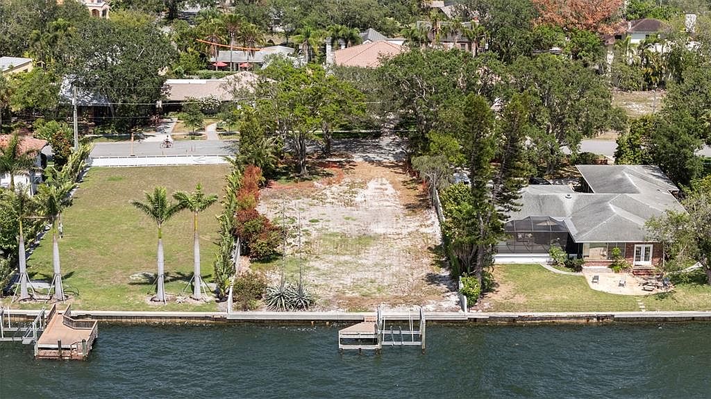 This aerial view showcases a waterfront property featuring a vacant lot and a neighboring house. The vacant lot has a cleared area with potential for building, while the adjacent house includes a screened-in porch and a dock. The waterfront location offers direct access to the water, enhancing the property's appeal.