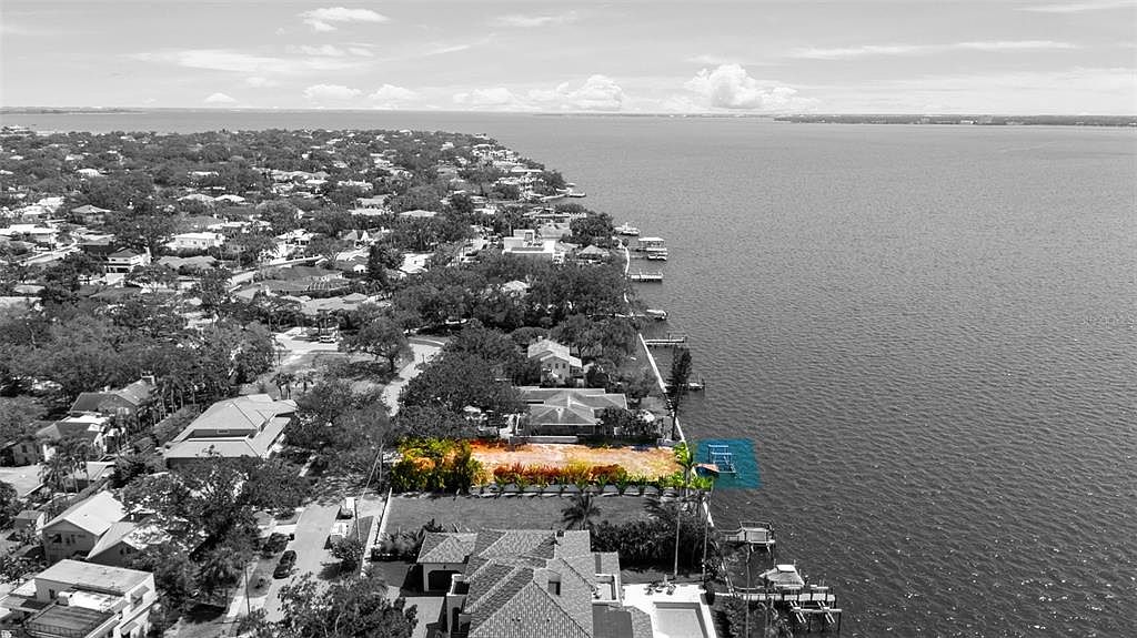 This aerial view showcases a waterfront property with a cleared lot ready for development. The surrounding neighborhood features mature trees and established homes, while the waterfront offers direct access to the bay. A private dock extends into the water, suggesting boating and recreational opportunities.