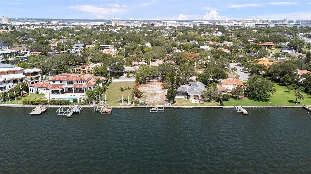 This aerial view showcases waterfront properties, highlighting their proximity to the water and the surrounding neighborhood. The image captures a mix of residential architecture, mature trees, and clear water, creating an appealing scene for potential buyers interested in waterfront living. The perspective gives a broad overview of the area, emphasizing the location's desirability.
