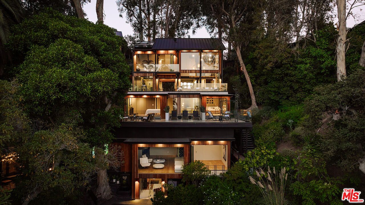 This aerial view showcases a modern, multi-story home nestled among lush trees. The house features large windows and balconies, offering stunning views and ample natural light. The architectural design emphasizes a connection with nature, creating a serene and private living environment.