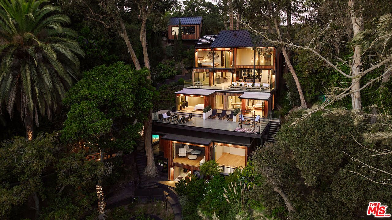 This aerial view showcases a modern, multi-level home nestled among lush greenery. The architectural design features extensive use of glass and wood, creating a seamless blend with the natural surroundings. Multiple decks and outdoor living spaces offer ample opportunities for relaxation and entertainment, enhancing the property's appeal.