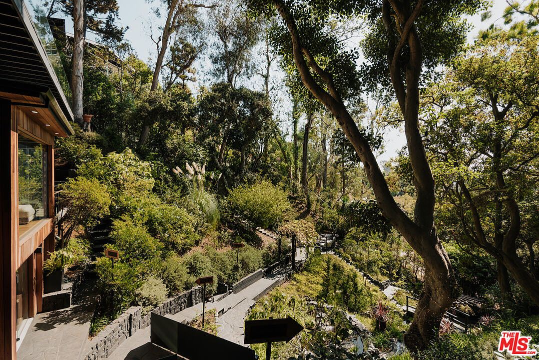 This image showcases a lush and meticulously landscaped yard or garden. A stone pathway winds through the greenery, leading the eye deeper into the property. The abundance of trees and shrubs creates a sense of privacy and tranquility, making it an appealing outdoor space.
