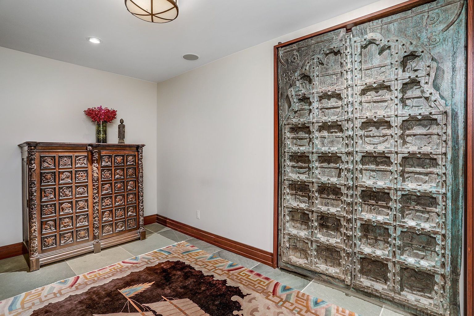 This interior shot showcases a hallway featuring a large, ornate wooden cabinet with carved details and a decorative rug. A striking, antique-style double door with intricate carvings adds a unique architectural element. The space is well-lit with recessed lighting and a decorative ceiling fixture, creating a sophisticated and inviting atmosphere.