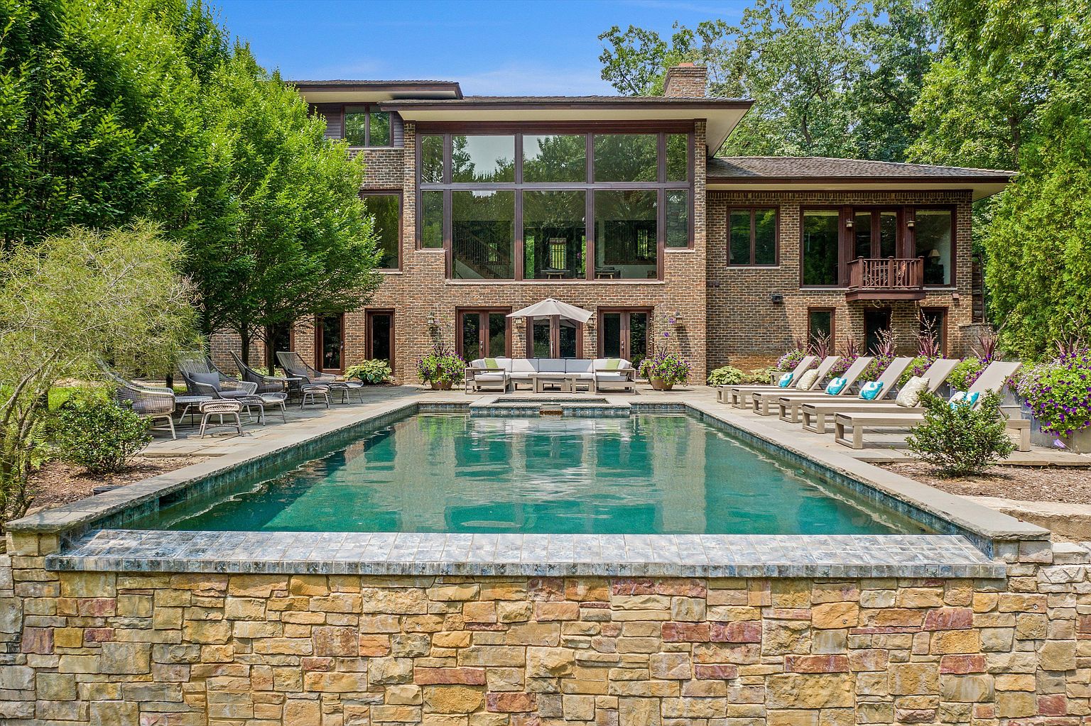 This image showcases a luxurious backyard pool area. The rectangular pool is surrounded by lounge chairs and lush landscaping, creating a serene and private oasis. The brick facade of the house provides a stately backdrop, enhancing the overall appeal of the outdoor space.