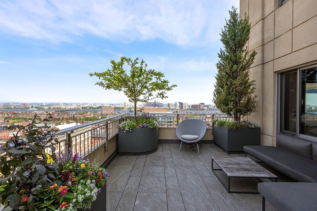 This image showcases a luxurious balcony with a stunning city view. The space is furnished with modern outdoor furniture, including a comfortable chair, a sleek sofa, and a stylish coffee table. Potted plants and trees add a touch of nature, creating a serene and inviting atmosphere.