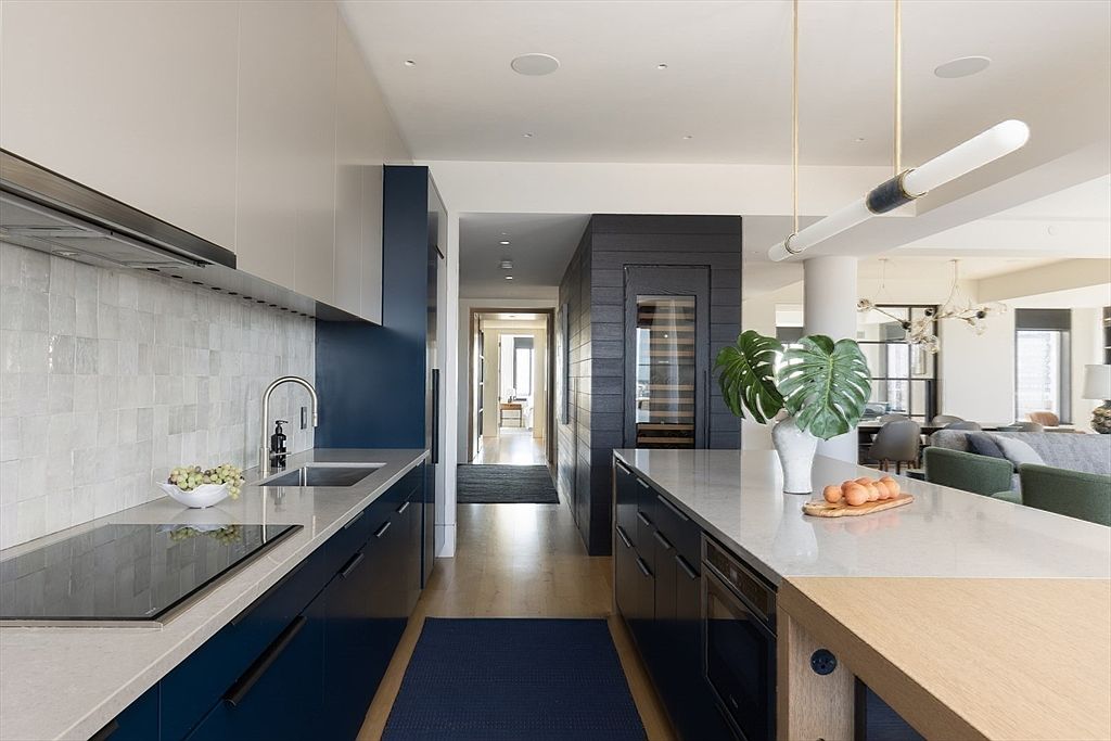 This is a modern kitchen with a sleek design, featuring dark blue cabinetry and light countertops. The kitchen island is topped with a light countertop and a wooden accent. The space opens into a living area, creating an open-concept feel.
