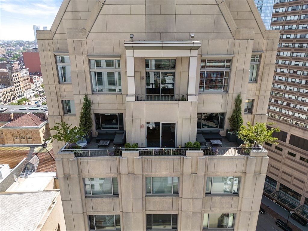 This aerial view showcases the upper floors of a luxury building, highlighting its architectural details and outdoor living spaces. The balconies are furnished with seating areas and greenery, offering a private retreat with city views. The building's facade features a combination of windows and textured panels, creating a sophisticated and modern aesthetic.